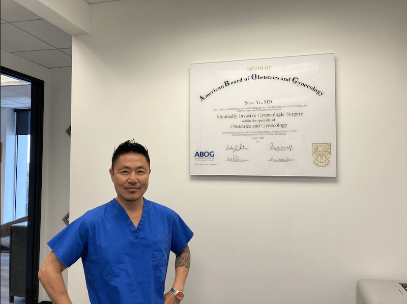 Dr. Yu standing beside his MIGS certificate.